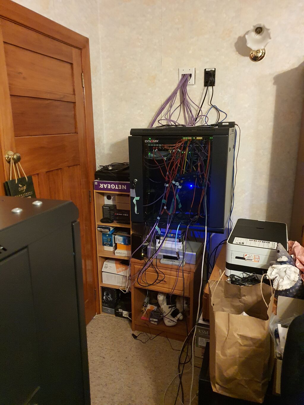 A small network cabinet replete with network gear and cables is mounted above a bedside dresser.