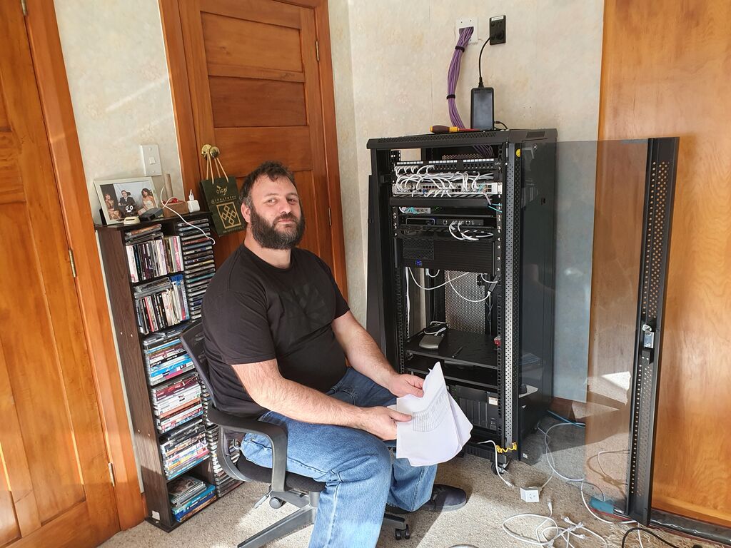 Richard Barlow, a bearded gentleman in jeans and T-shirt, adjusts a cable in some network gear in a newly-furnished larger network cabinet.
